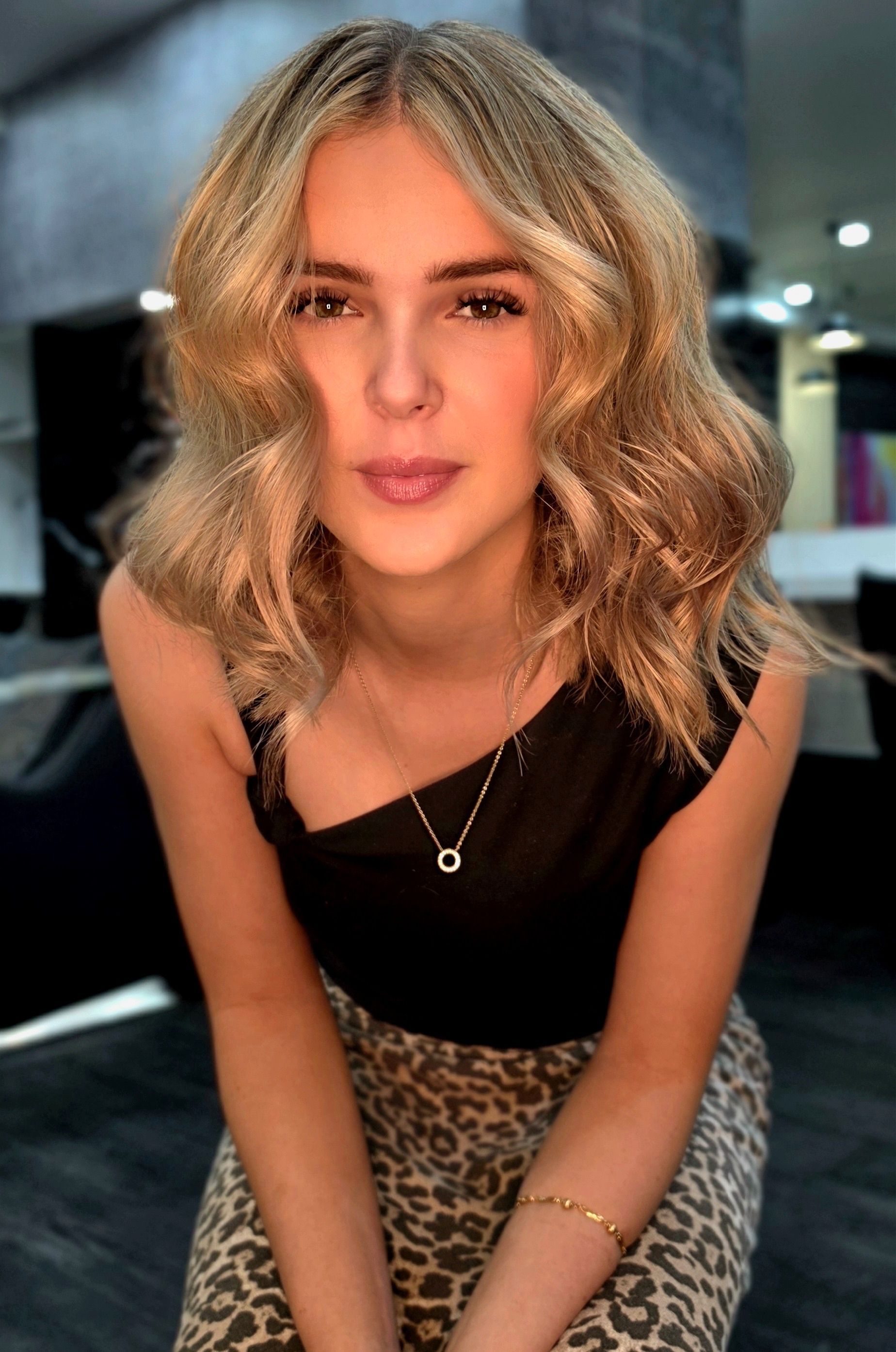Portrait of a woman with wavy blonde hair, wearing a black top and leopard-print pants, indoors
