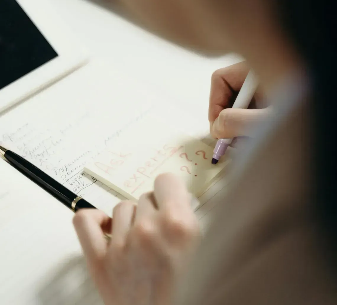 Person writing notes in a notebook beside a laptop on a desk.