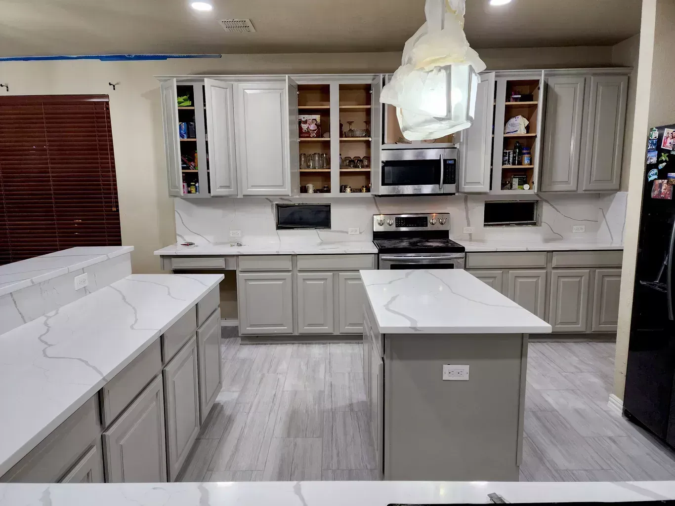 Bright kitchen with white cabinets, marble counters, island, and pendant light.