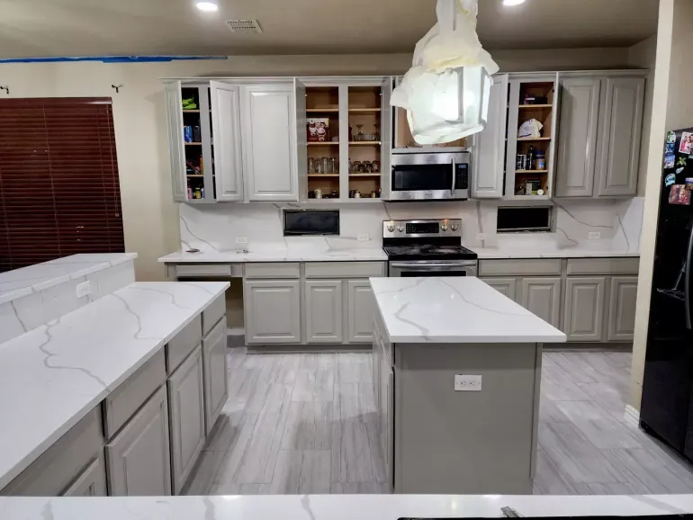 Modern kitchen with white cabinets, marble countertops, island, and stainless steel appliances