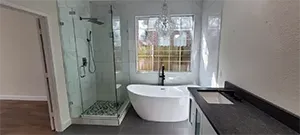 Modern bathroom with glass shower, freestanding tub, and black vanity by a window
