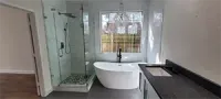 Modern bathroom with glass shower, freestanding tub, and black vanity by a window