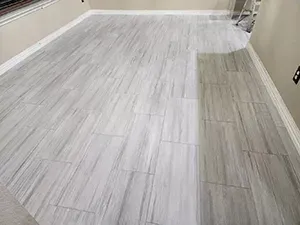 Empty room with light gray wood-look flooring and beige walls, showing a small section of darker flooring on the right.