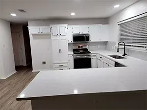 Empty modern white kitchen with island, stainless-steel appliances, and window blinds