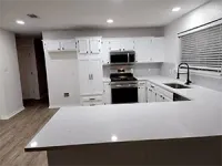 Empty modern white kitchen with island, stainless-steel appliances, and window blinds