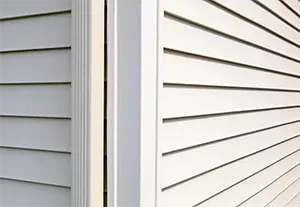 Close-up of two house exteriors meeting at a corner, with white and gray vinyl siding and trim.