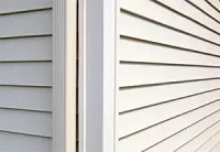 Close-up of two house exteriors meeting at a corner, with white and gray vinyl siding and trim.