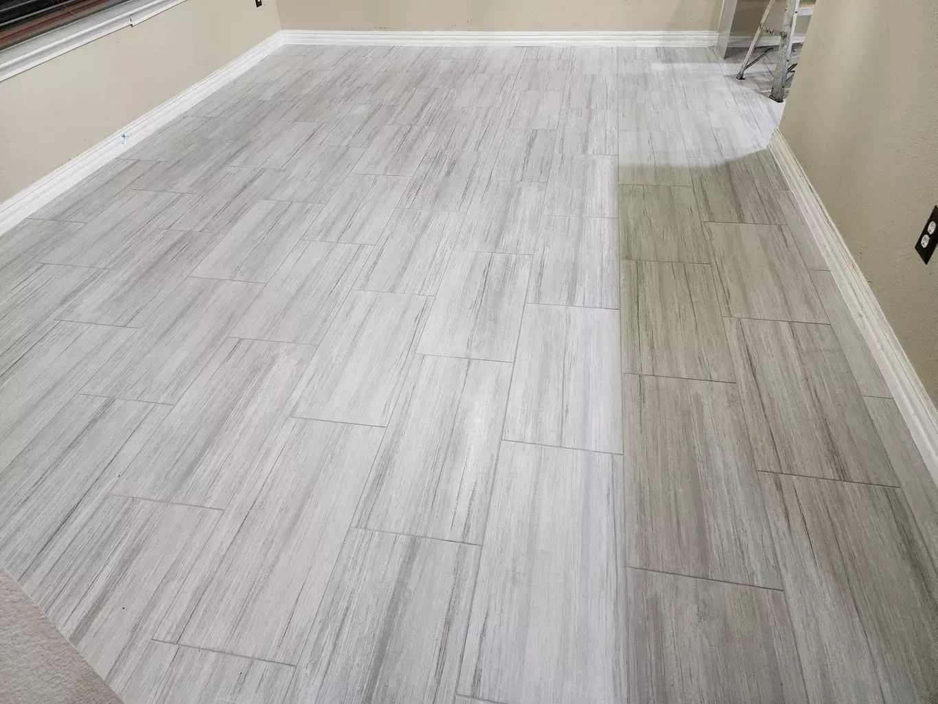 Empty room with light gray wood flooring and beige walls, showing a narrow darker strip along one side.