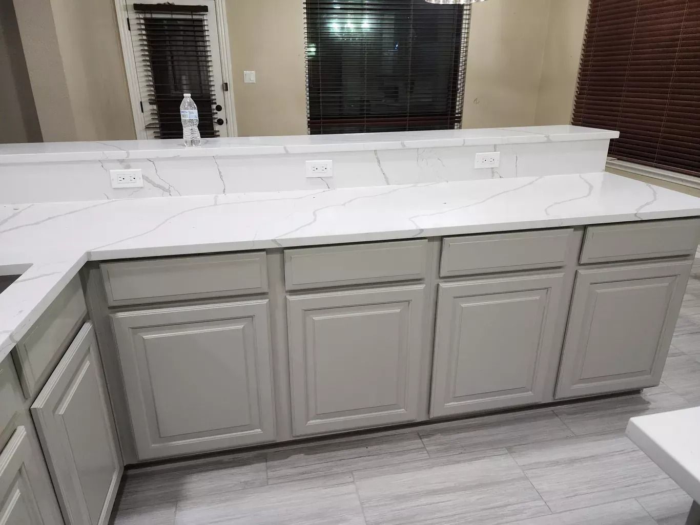 Bathroom vanity with double sink, white countertop, and light gray cabinet doors beneath a mirror.