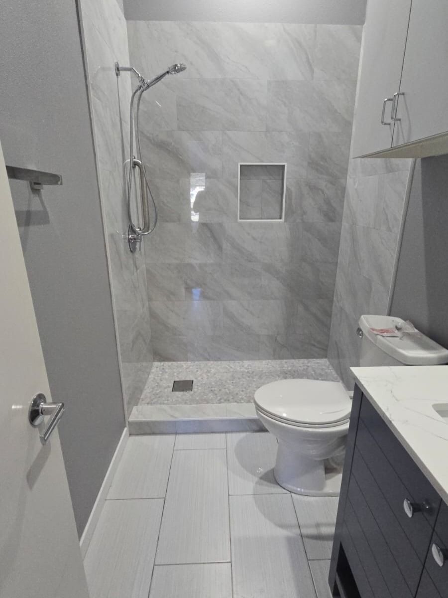 Small modern bathroom with shower, toilet, gray tile walls, and a vanity sink.