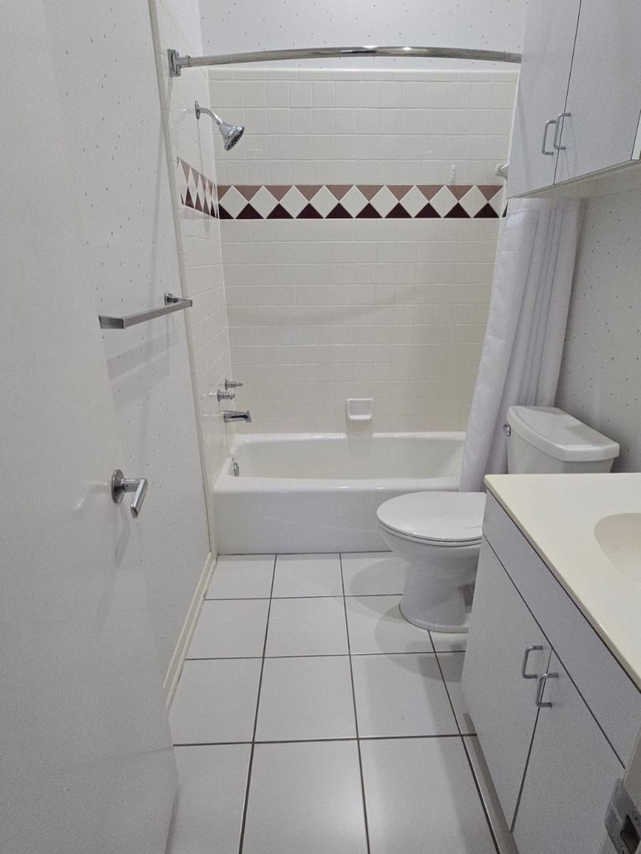 Small white bathroom with a bathtub, toilet, sink, and tiled floor.