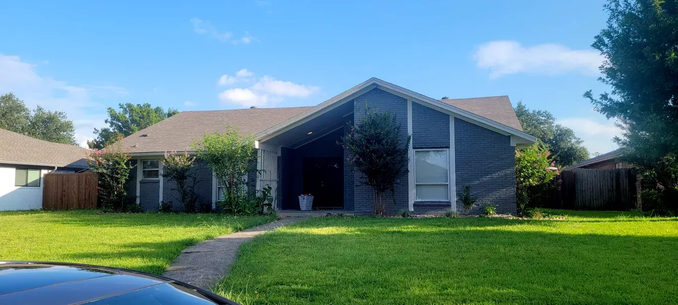 Single-story suburban house with brick front, wide lawn, and clear blue sky
