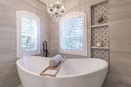 Bright bathroom with a freestanding tub, chandelier, and two windows with patterned tile accents