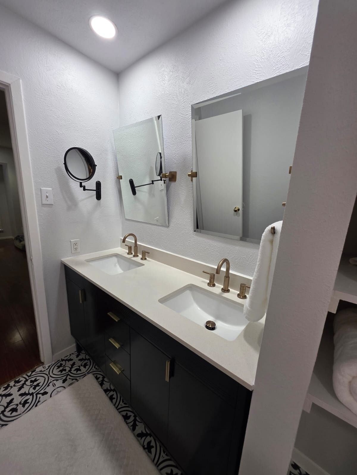 Modern bathroom vanity with double sinks, large mirror, and patterned black-and-white floor tiles.