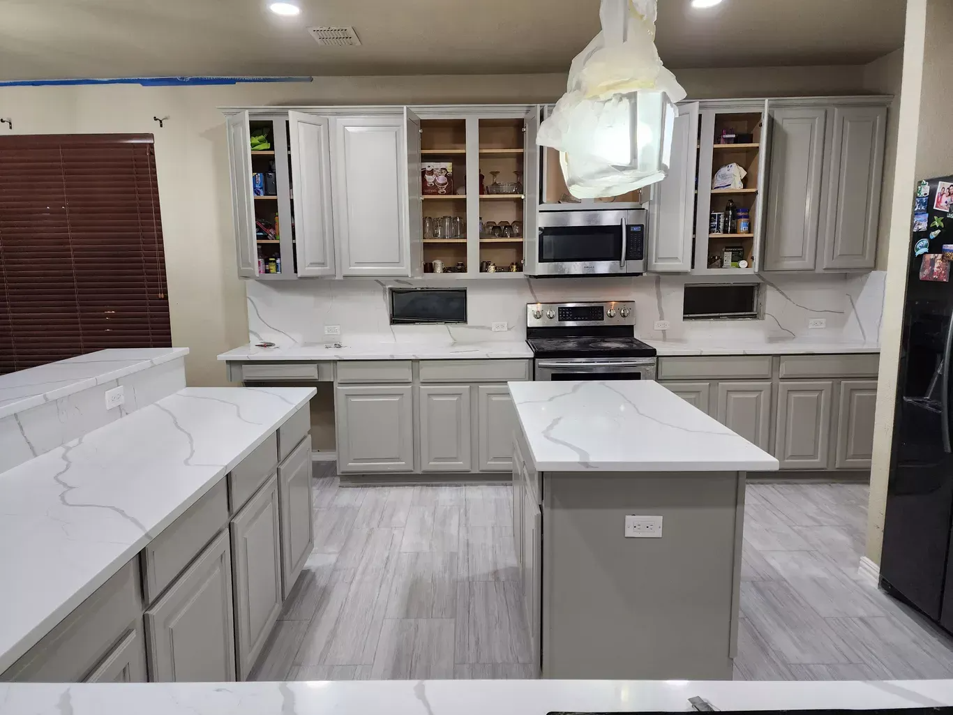 Bright modern kitchen with white cabinets, marble countertops, and a central island under a hanging light fixture