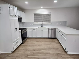 Bright modern kitchen with white cabinets, stainless appliances, and wood-look flooring