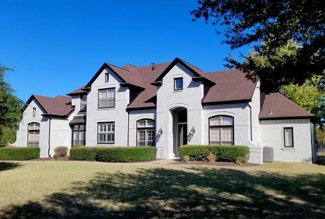 Large white stucco house with brown roof and arched entry, fronted by a grassy lawn under a blue sky