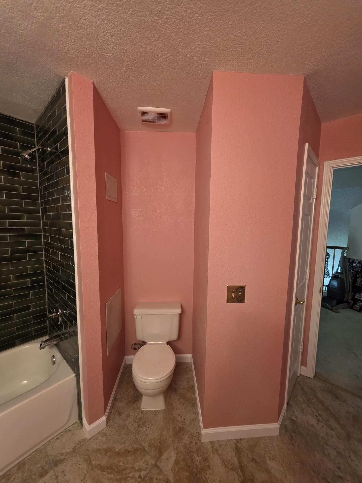 Small bathroom with pink walls, toilet, bathtub on left, and doorway to a hall on the right