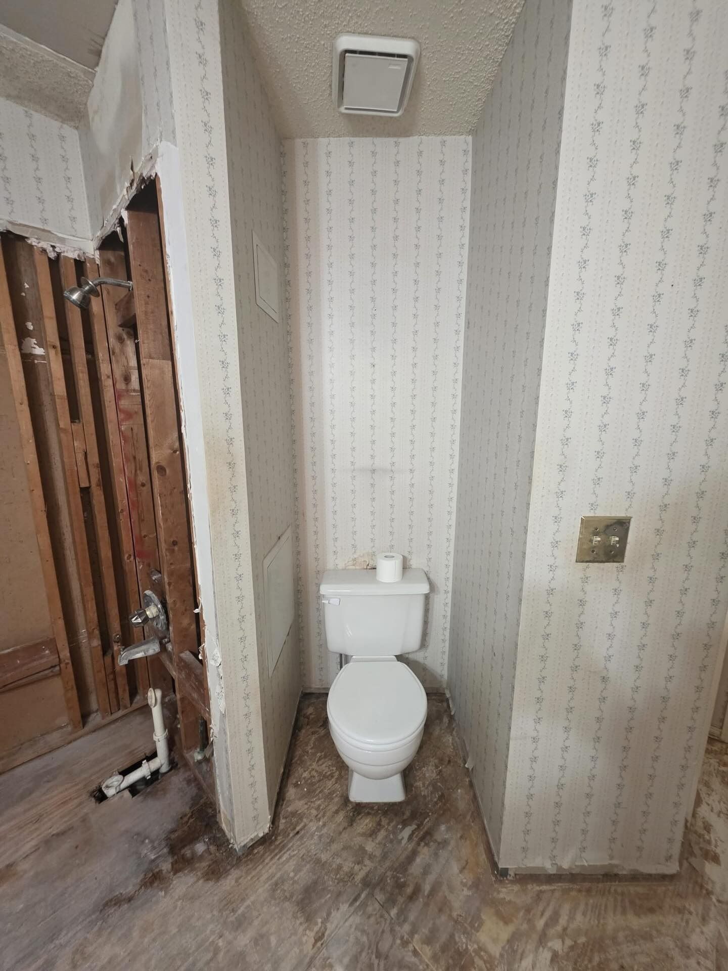 Small bathroom with a toilet in a narrow alcove, patterned wallpaper, and wood flooring.
