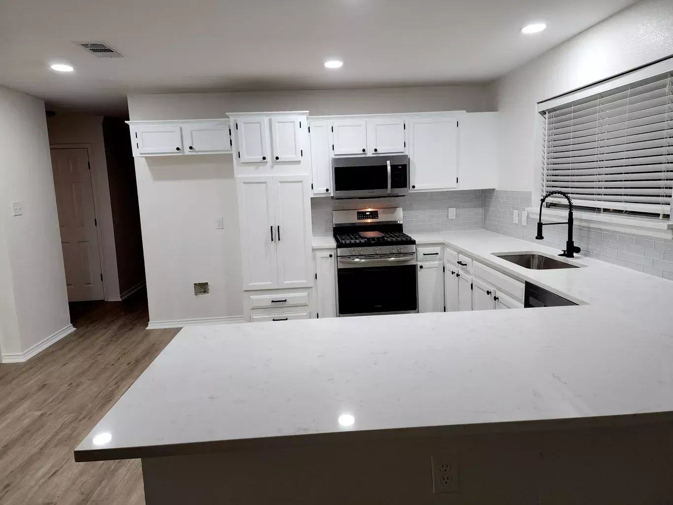 Empty modern white kitchen with island, cabinets, stainless oven, and window blinds at night