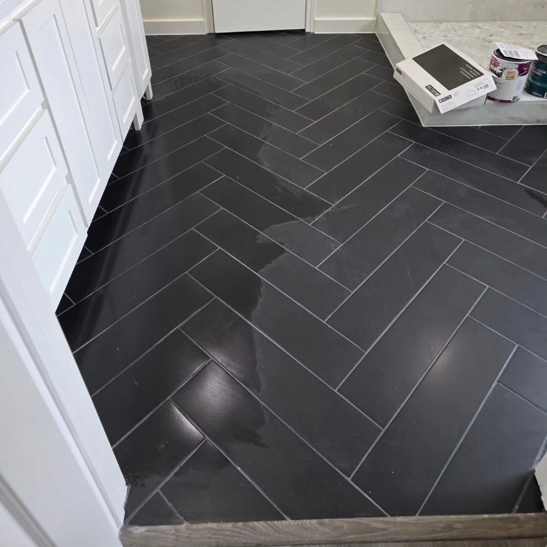 Black herringbone tile floor in a room with white cabinets and a small tray near the wall.