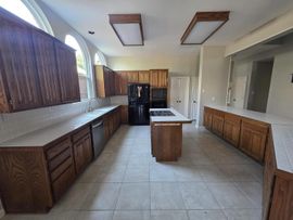 Empty kitchen with dark wood cabinets, white tile floor, central island, and large windows.