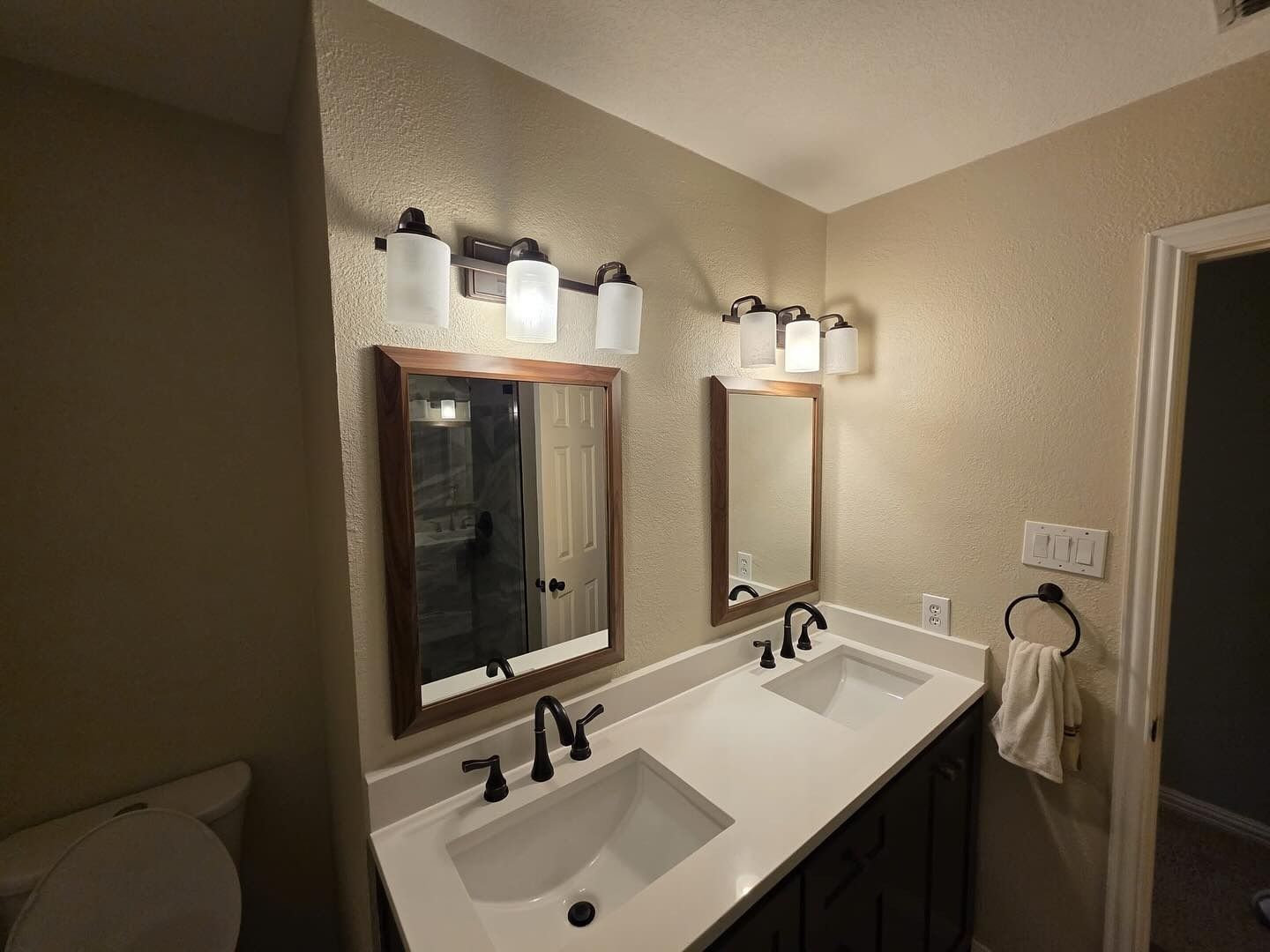 Small beige bathroom vanity with double sinks, mirrors, and wall lights above a white countertop.
