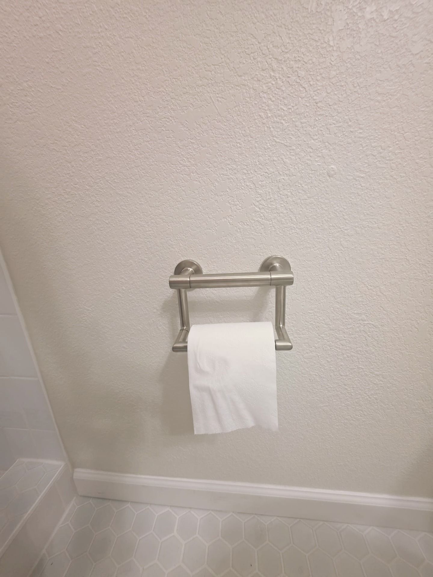 Toilet paper roll on a chrome wall-mounted holder in a bathroom.