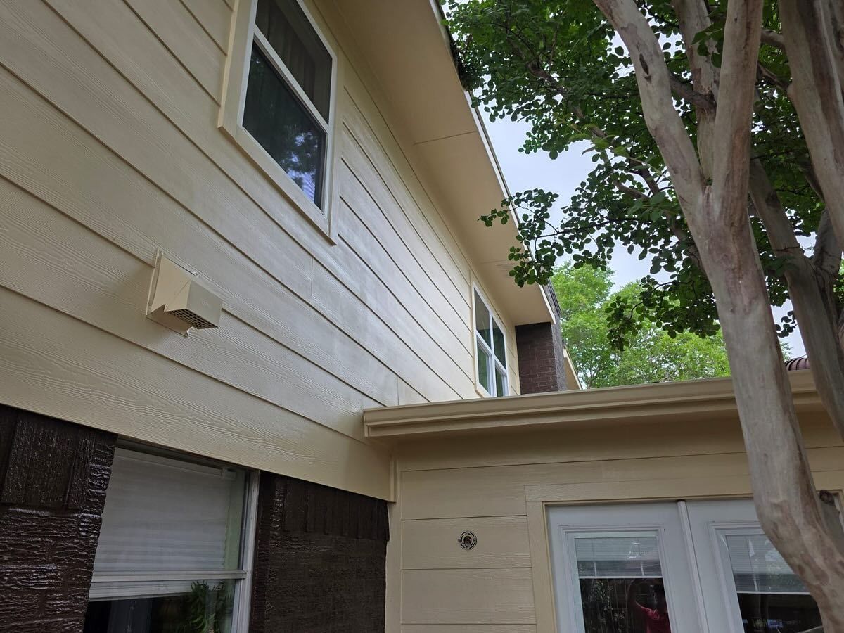 Exterior of a beige house with windows, a tree, and leafy branches overhead