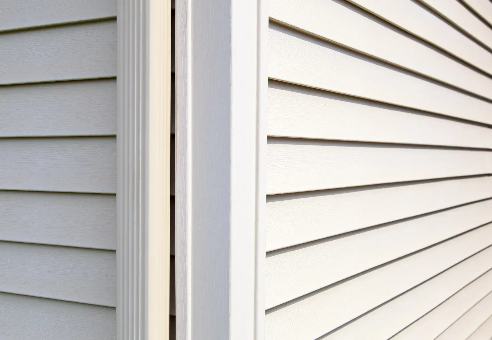 Close-up of a white house corner with gray and white vinyl siding panels.