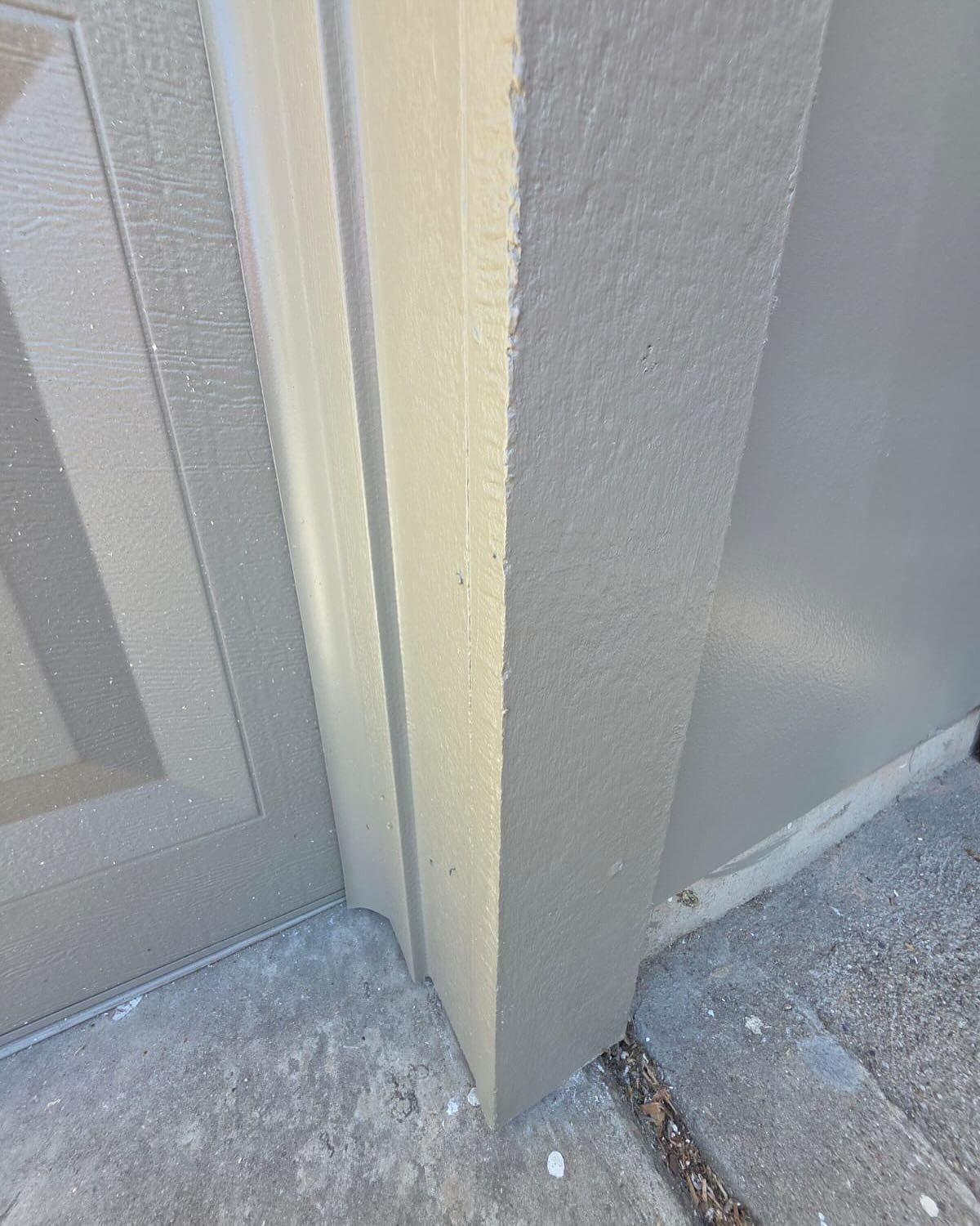 Close-up of a beige door frame and gray wall corner with a cracked concrete floor edge.