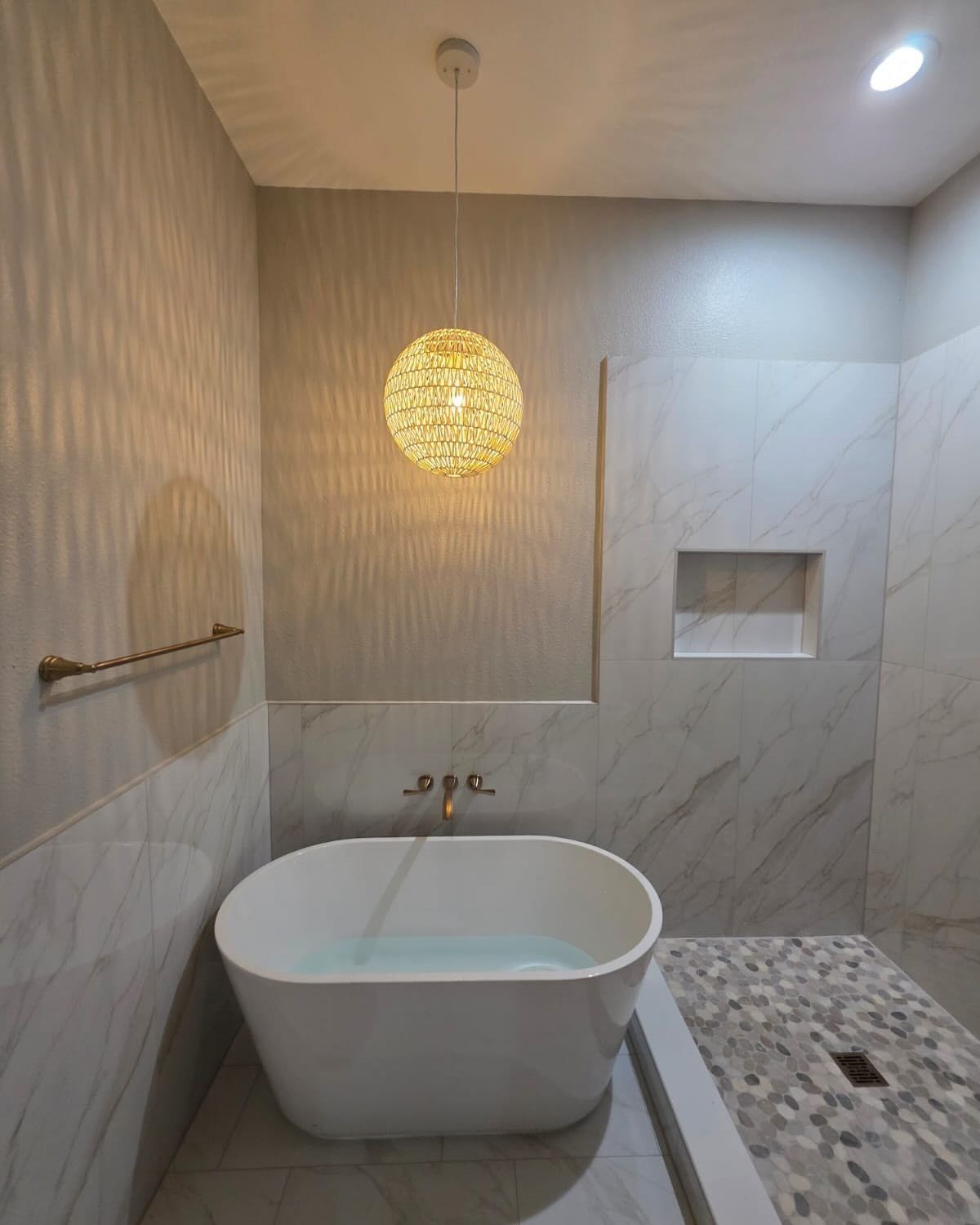 Modern bathroom with freestanding tub, tiled walls, pendant light, and open shower area