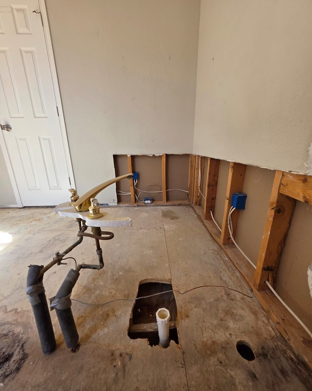 Partially stripped bathroom with exposed wall studs, plumbing pipes, and a tub drain opening on the floor