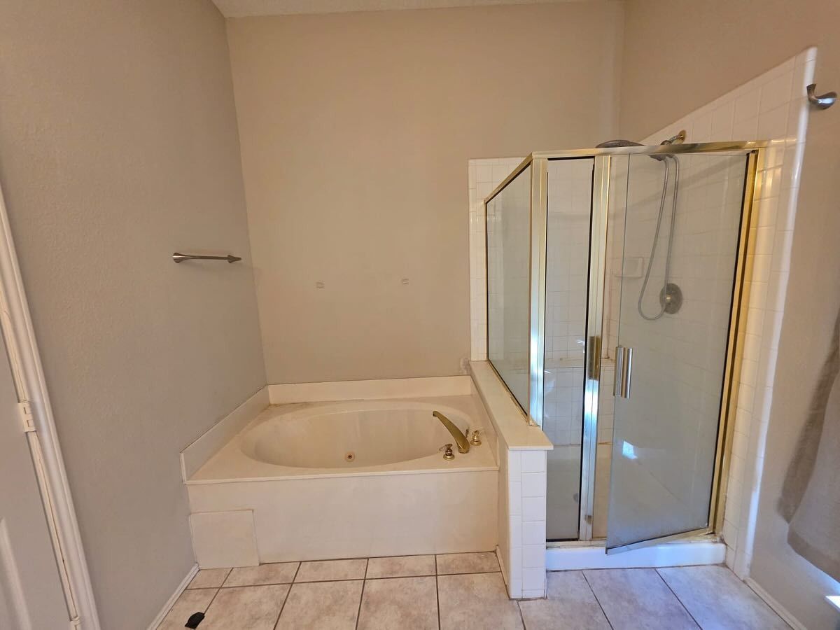 Bathroom with white tiled corner bathtub and glass shower enclosure, seen from the doorway.