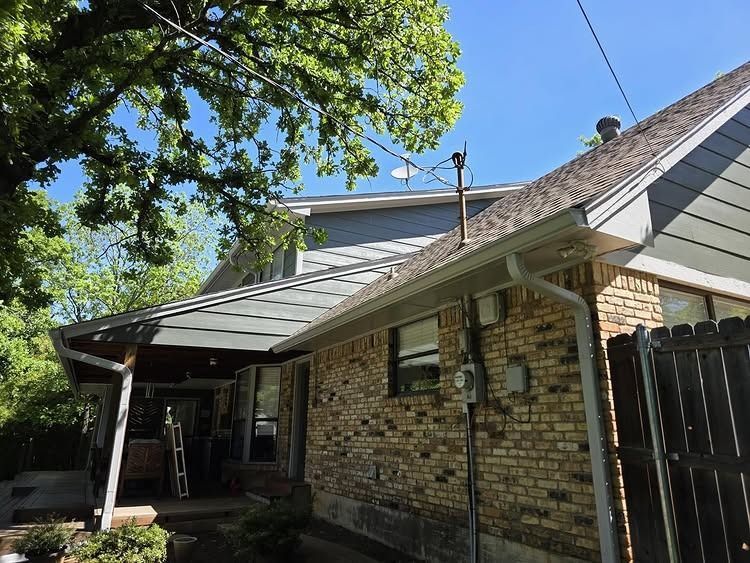 Brick house exterior with gray roof, covered patio, and leafy tree in the foreground