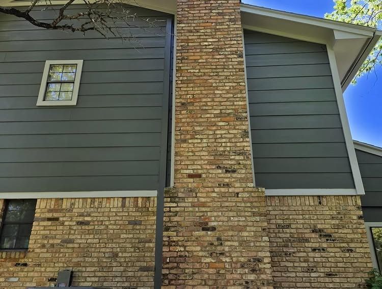 Brick house exterior with dark gray siding, central chimney, and a small window under a blue sky