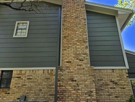 Brick house exterior with dark gray siding, central chimney, and a small window under a blue sky
