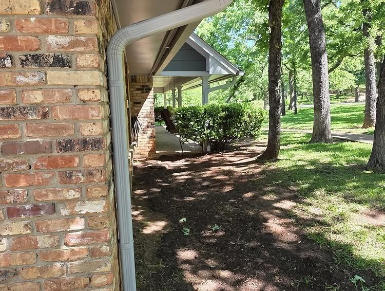 Brick house side yard with trees, shaded grass, and a covered porch gutter in view