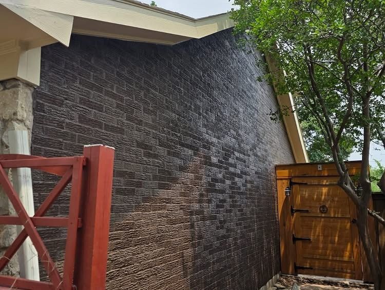 Dark brick wall beside a wooden gate, with red fence and tree branches overhead.