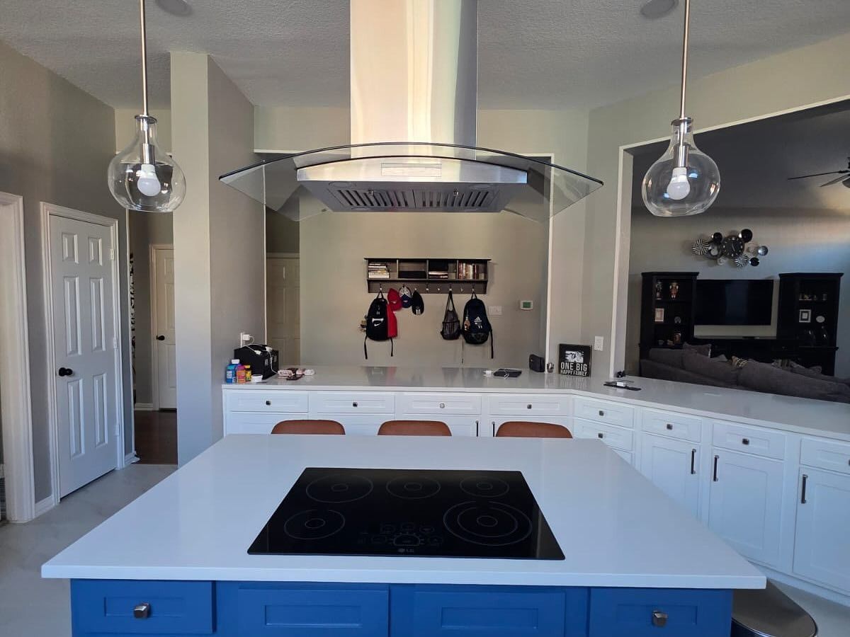 Modern white kitchen with island, stainless range hood, pendant lights, and black cooktop.