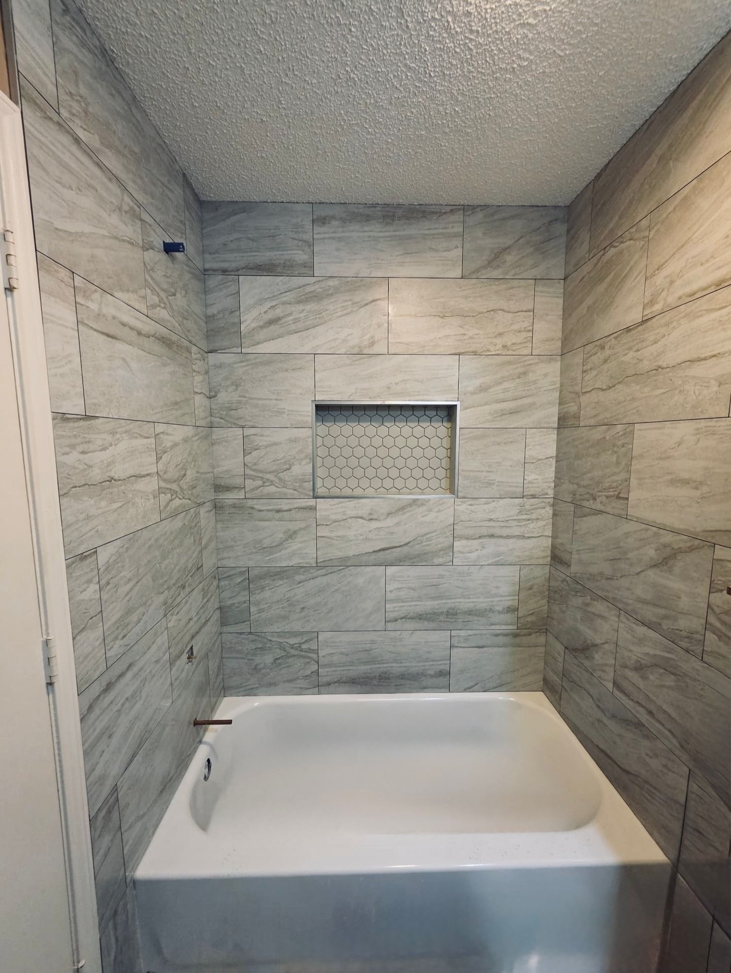 Tiled bathroom alcove with a white soaking tub and a recessed wall niche above it.