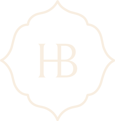 Monogram “HB” in pale gold inside a thin ornate floral border on a white background
