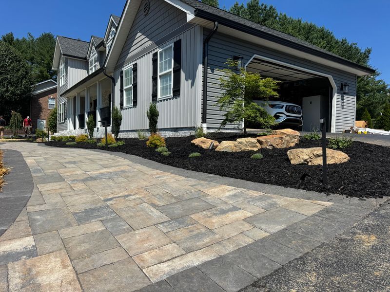 Modern gray house with stone driveway, garage, and landscaped front yard on a sunny day