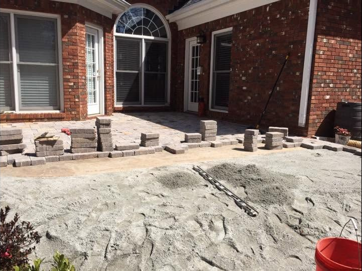Brick house patio under construction with stone pavers and a rough gravel foreground