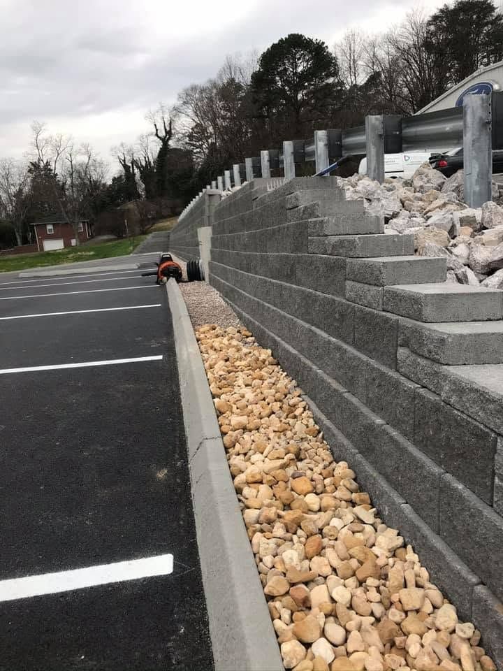 Parking lot beside stepped stone retaining wall with rocks and a person crouching near the wall.