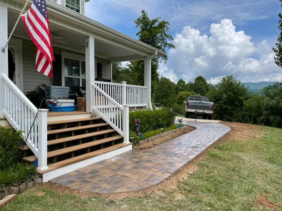 Front porch with stairs, American flag, and curved stone walkway leading to a driveway.