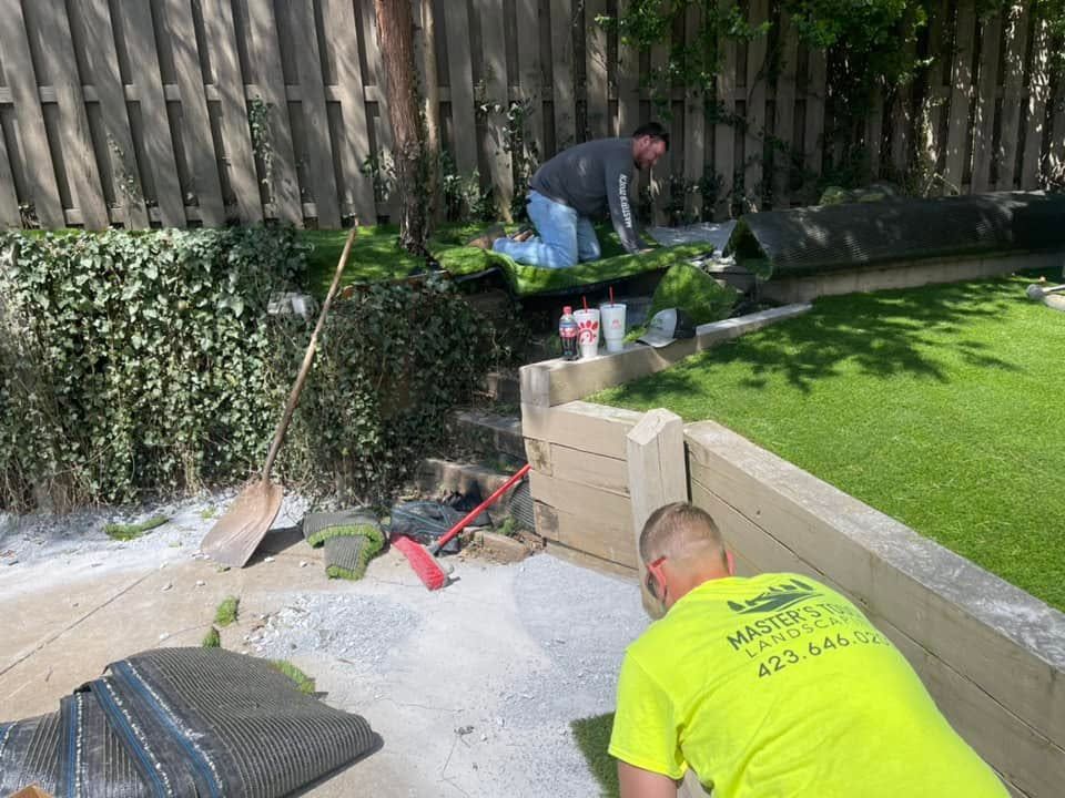 Two workers cleaning a backyard patio beside a lawn and stone planter.