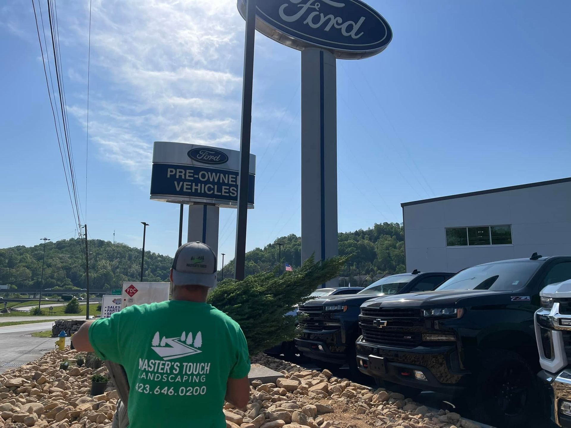 Man in green shirt walking toward a Ford dealership lot with parked SUVs and a blue sky.