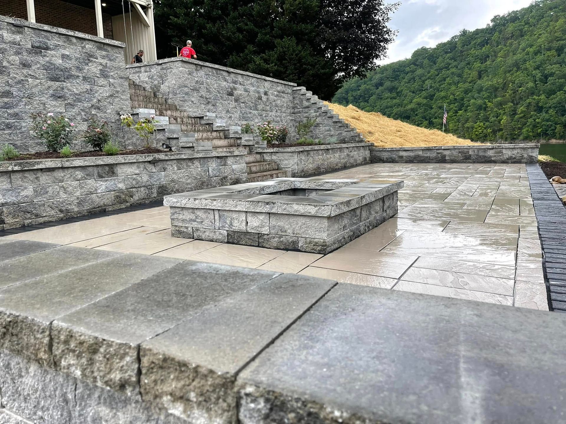 Stone terraces and steps beside a wet courtyard with a forested hillside in the background