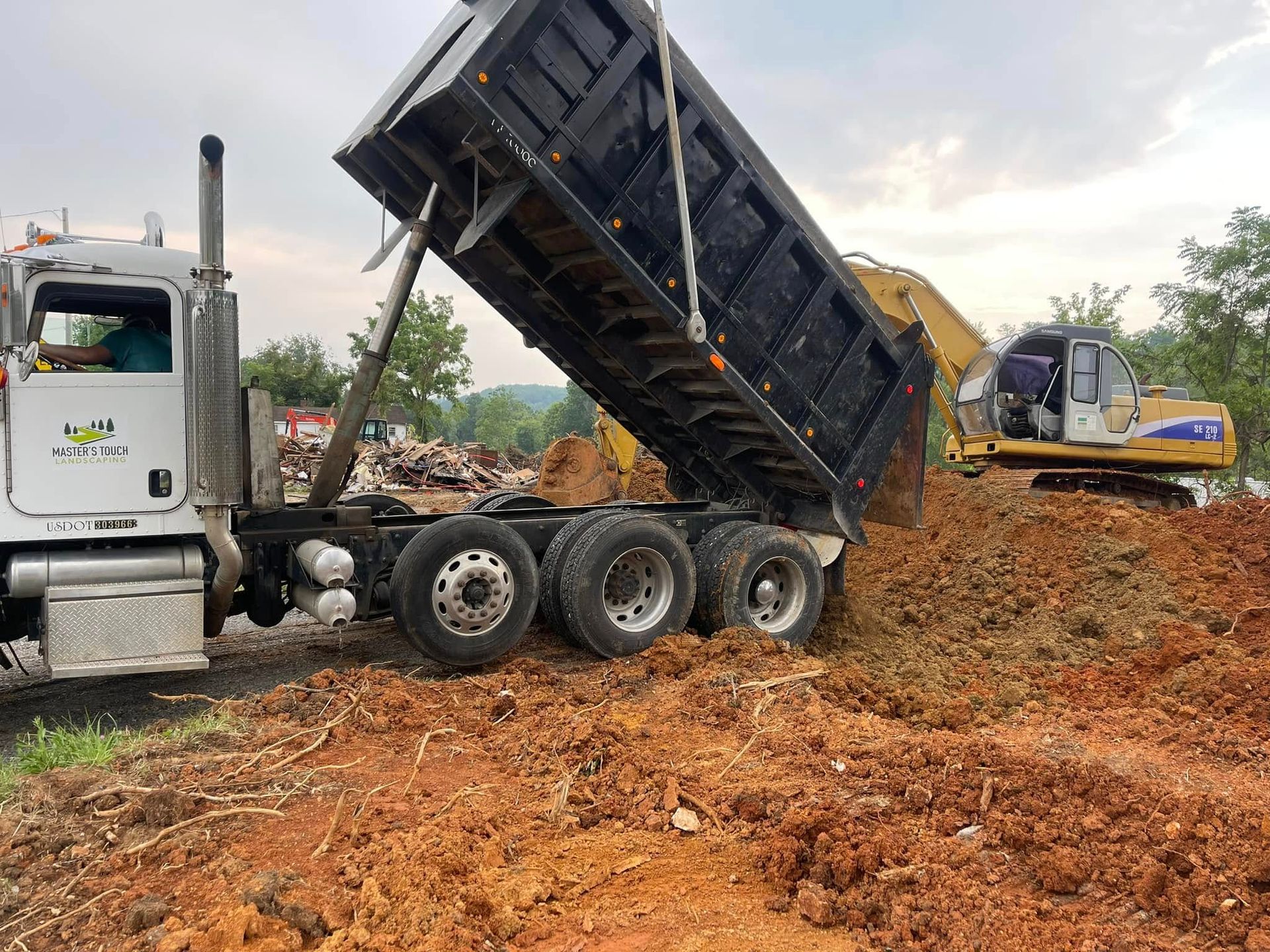 Dump truck unloading dirt beside an excavator at a muddy construction site